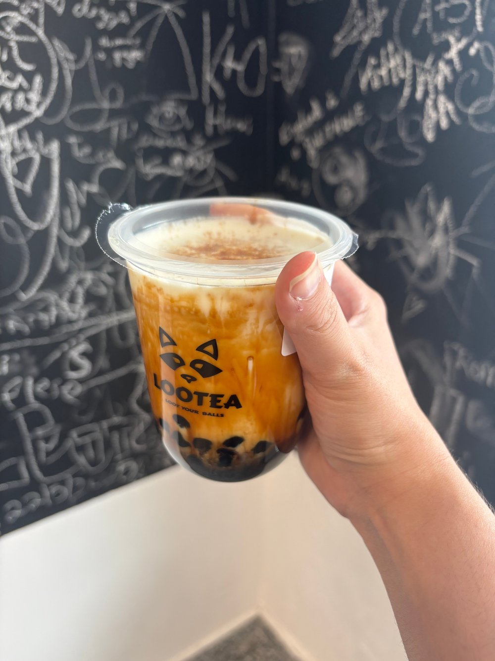 A Lootea Brown Sugar drink held in front of the message-covered blackboard, photographed by Ranya E.